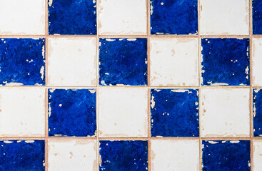Detail of a wall of the interior of a ruined house with white and blue square tiles.