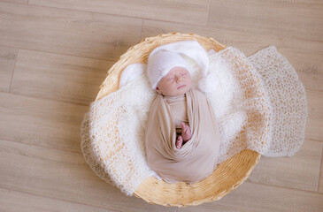 Cute little baby in white knitted hat  lies in a wicker basket  in a beige knitted blanket. Summer mood. Happy healthy childhood