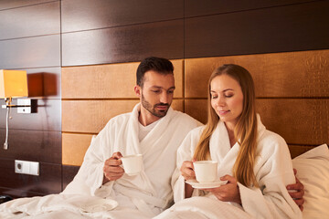 Obraz premium Joyful couple with hot drinks in bed