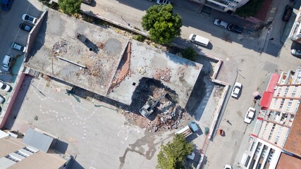 Aerial view of excavator demolishes an old building in city center. Water truck squeezes water to suppress the smoke. 