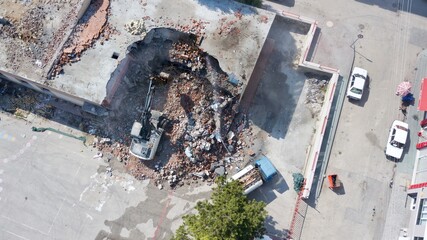 Aerial view of excavator demolishes an old building in city center. Water truck squeezes water to...