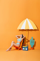 happy woman with closed eyes sitting on deck chair near paper boombox, cactus and umbrella on orange