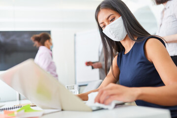 Geschäftsfrau mit Gesichtsmaske beim Tastatur desinfizieren