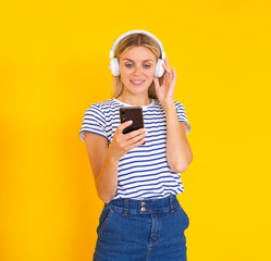 Unlimited music app. Smiling girl with headphones listening to the music on her phone on a yellow background