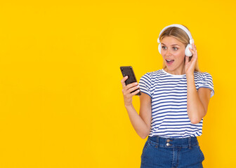 Music app mockup. Shocked young woman with headphones listening to the music on her phone on a yellow background with copy space for your tariff plans and app promo