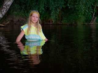 blonde girls with blue eyes bathes in clothes in the dark water of a lake at sunset