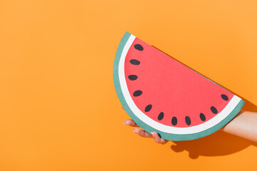 cropped view of woman holding paper cut watermelon on orange