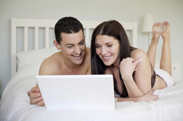 Couple lying forward on the bed using laptop
