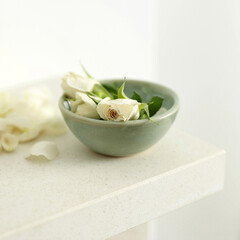 A bowl of white roses with a few petals scattered beside the bowl