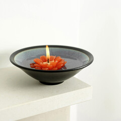 A bowl of water with lit candle floating on it