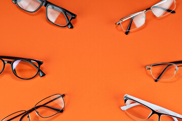 Different types of glasses on an orange background close up. Glasses with rectangular and round frames. Layout for design. Space for text and free space near the object. - obrazy, fototapety, plakaty