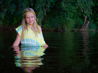 blonde girls with blue eyes bathes in clothes in the dark water of a lake at sunset