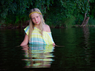 Fototapeta premium blonde girls with blue eyes bathes in clothes in the dark water of a lake at sunset