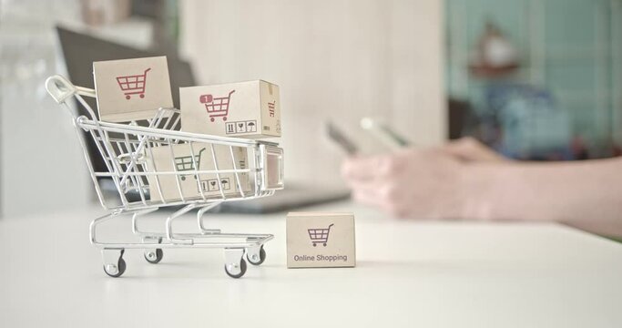 Online shopping / ecommerce and delivery service concept : Box or cartons in a shopping cart or trolley, buyer or customer uses smartphone to order things from retailer sites and pay by a credit card