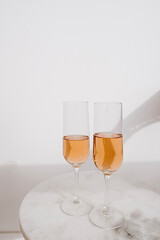 Cheers! Two glasses of rose champagne in sunlight shadows on marble tablet against white wall. Happy Birthday, anniversary party holiday celebrating decoration festive concept