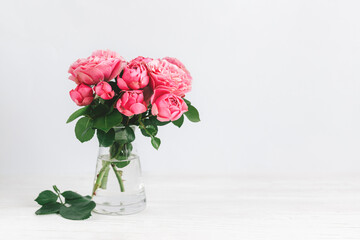 Romantic bouquet of pink roses in a glass vase on a white background.
