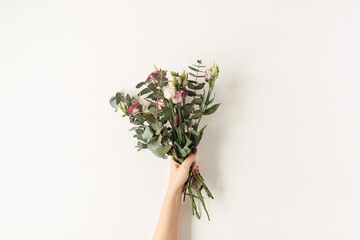 Female hand holding colorful roses flowers bouquet against white wall. Holiday celebration festive floral concept