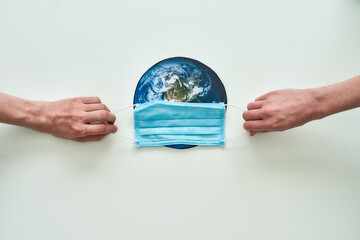 Conceptual flatlay with hands holding medical mask on planet Earth made of paper over white background. Quarantine and protection against coronavirus concept.