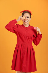 Cute Asian woman in red dress holding macaron over orange background.