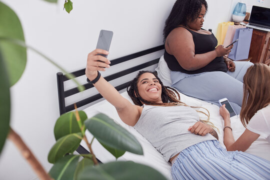Young lady of mixed race taking picture of herself resting indoors with her friends