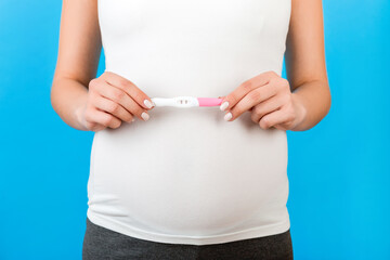 Cropped image of pregnant woman in home clothing showing positive pregnancy test with two stripes at blue background. Healthy pregnancy. Copy space