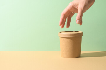 Craft paper soup cup and female hand on brown background. Ecological individual package. Zero Waste.