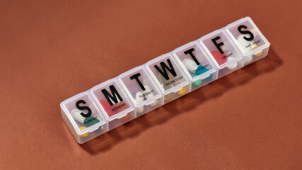 A weekly medicine dispenser, prescription pills and vitamins in a white pill box on terracotta background. Health care, vitamins and treatment concept