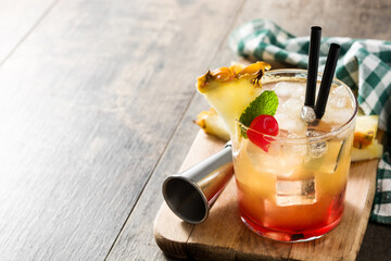 Cold mai tai cocktail with pineapple and cherry on wooden table. Copy space	
