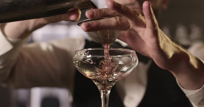 Close-up shooting. The bartender is pouring the alcohol from the shaker through a cocktail strainer into the glass. 4k