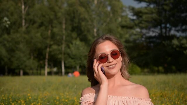 portrait of a beautiful stylish girl in summer clothes who is sitting in a park on the lawn and talking on the phone, free space for text hd stock footage