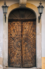 Old wooden brown door with ray pattern. Facade of gray stone with lanterns in the castle portal.