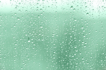 Rain drops on window glasses surface. Green abstract background of raining waterdrops. Natural Pattern of raindrops