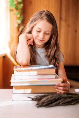 A smiling little girl sits leaning on a stack of books and textbooks, preparing to go back to school