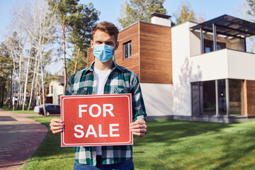 Happy male standing with sale sign near his new home