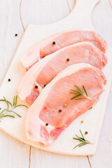 Raw pork fillet and rosemary on a white board top view.