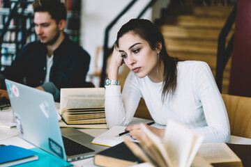 Bored young woman watching tutorial online on laptop computer preparing coursework project in college library, unhappy female student tired with learning disappointed with bad