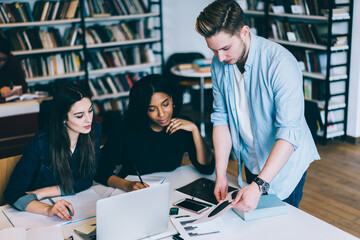 Young male communicating with female colleague planning project together on meeting,diversity crew of students making research and discussing ideas for coursework sitting at desktop in campus