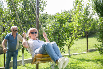Naklejka na ściany i meble Vertical image of a mature couple in-love on a tree swing outside