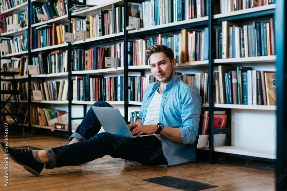 Poster portrait of successful young man student smiling at camera while keyboarding text for course work on