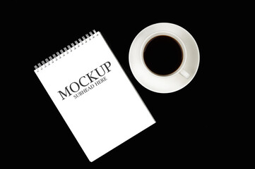 mockup of a white notebook with a white cup of coffee on a black background