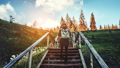 Fototapeta na wymiar Young girl hiker walking on a stairway with backpack in the mountains landscape at sunset. Lifestyle wanderlust adventure. Location Carpathian national park, Ukraine, Europe