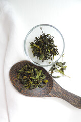  dry green tea leaves on a wooden spoon  and on a glass plate    