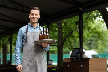 Work a waiter. Smiling handsome man in apron holds tray with bottles of beer in hands