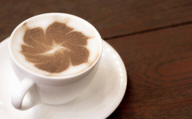 Close up flower pattern of cappuccino latte art in white ceramic cup on wooden table floor