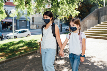 Two sisters going to school at the beginning of the year with masks on their faces