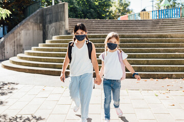 Two sisters going to school at the beginning of the year with masks on their faces