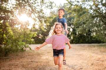 Happy children boy and girl frolic in the Park. The older brother plays with his sister in nature...