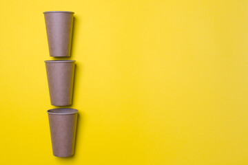 three eco-friendly cardboard cups lie on a yellow background with copy space. Mock-up. Close-up