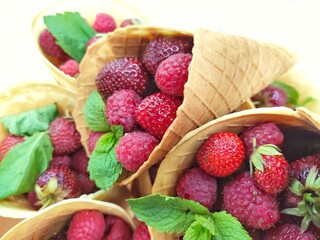 raspberries and strawberries with mint leaves in a waffle cone on a white background
