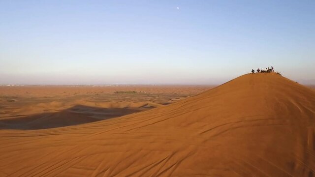Group of people standing on big golden sand dune, wide drone pulling back revealing landscape